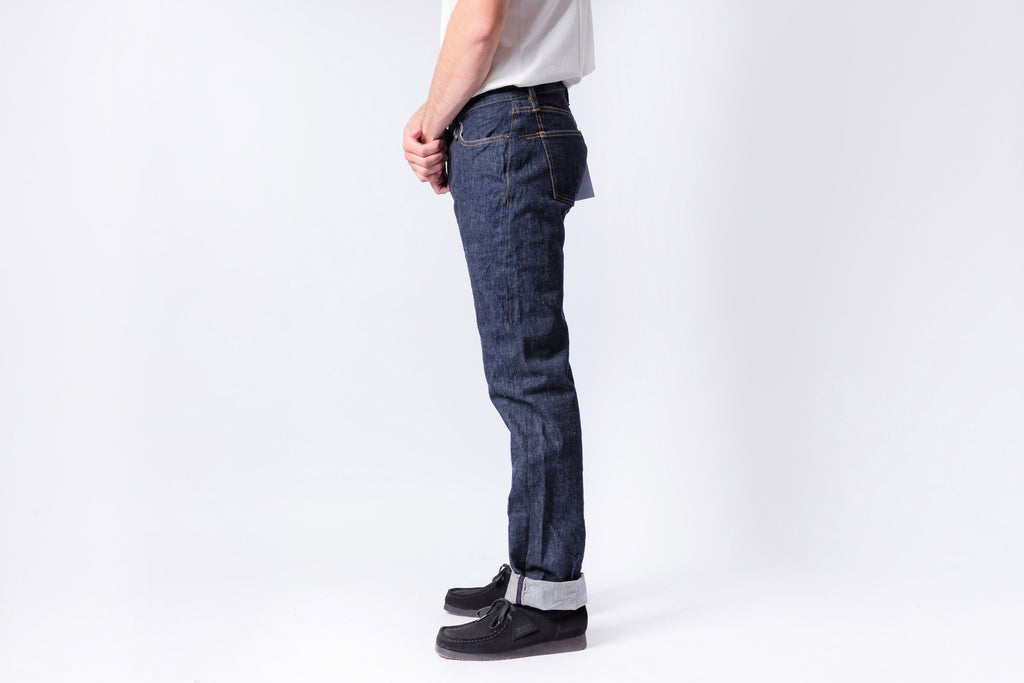 Person wearing dark blue jeans and black shoes on a white background