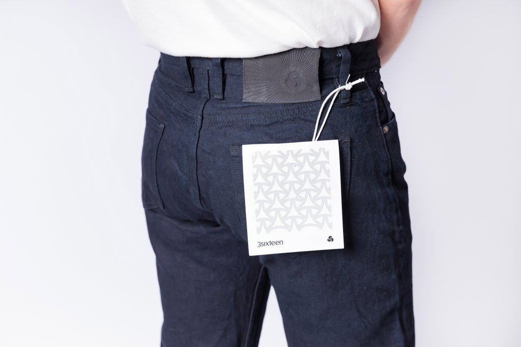 Person wearing dark pants with a brand tag on a white background