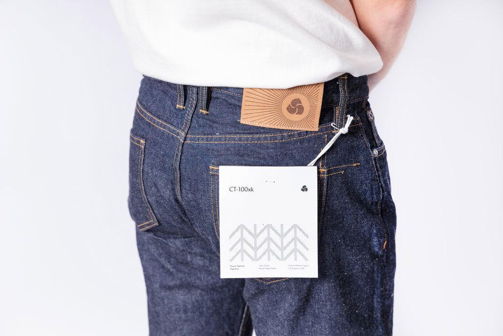 Person wearing blue jeans with a visible brand label on a plain background