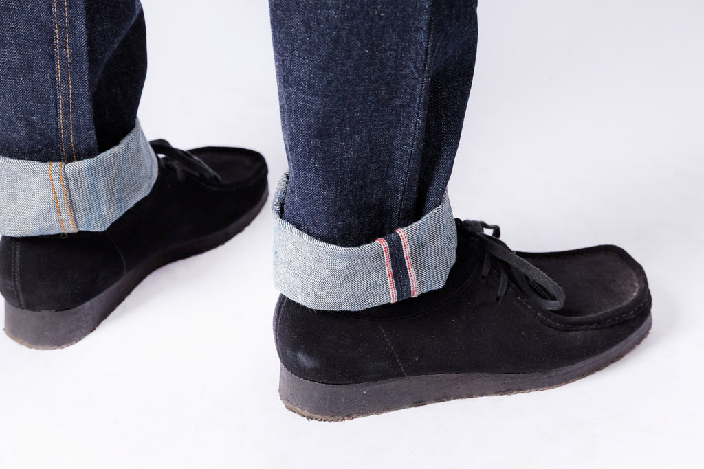 Black shoes worn with rolled-up jeans on a white background
