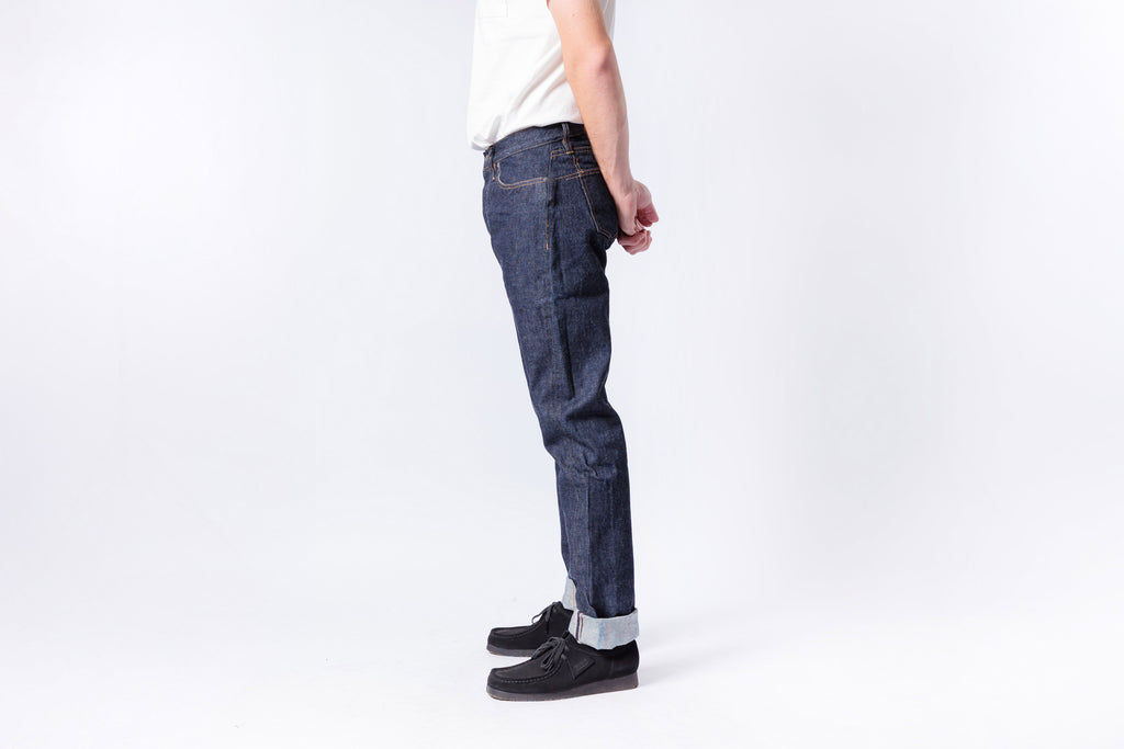 Person wearing dark blue jeans and black shoes on a white background