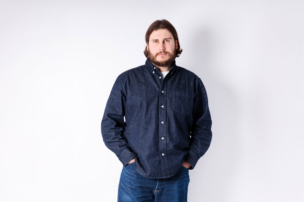 Man wearing a dark blue denim shirt and jeans against a white background