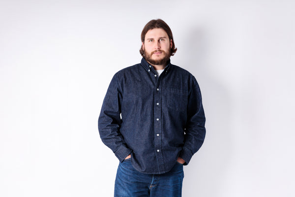 Man wearing a dark blue denim shirt and jeans against a white background