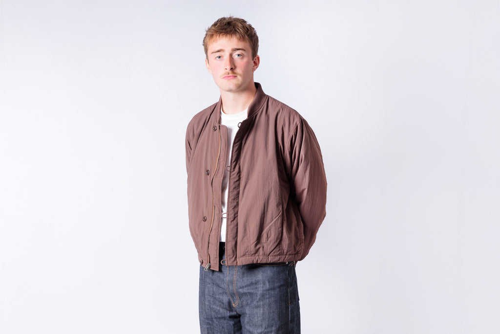 Man wearing a brown jacket and jeans on a white background