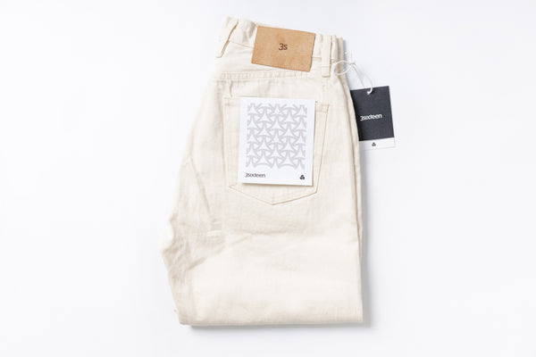 Folded cream-colored jeans with tags on a white background