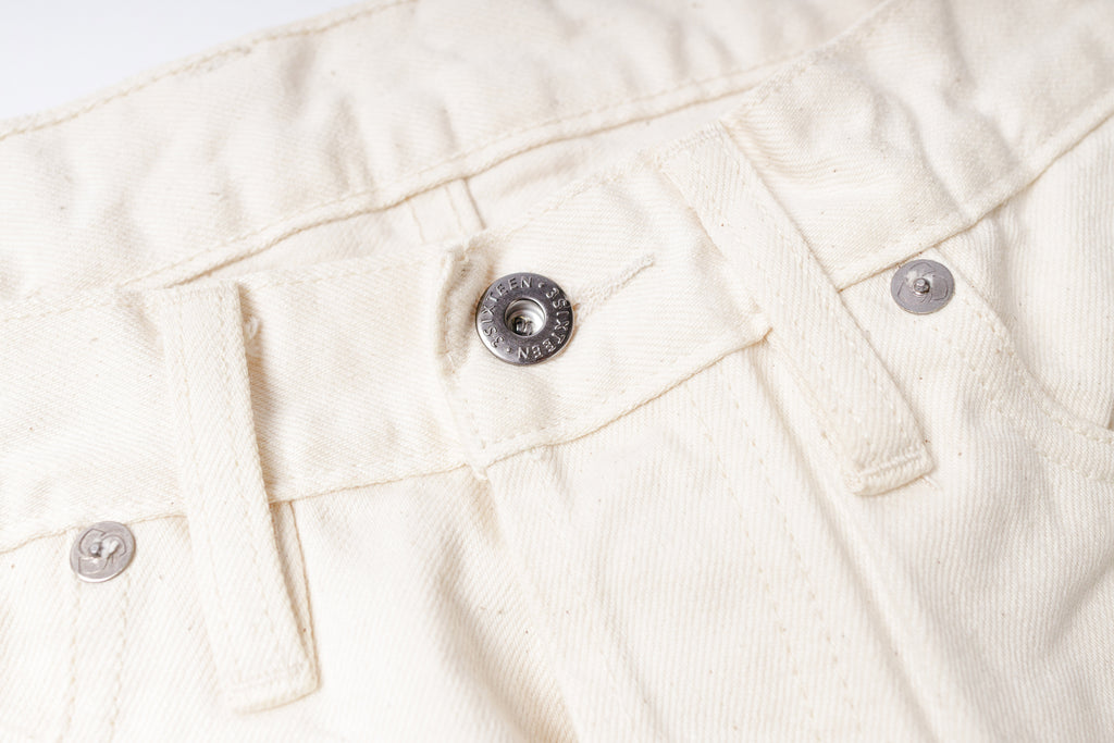 Close-up of a white denim fabric with button details on a light gray background