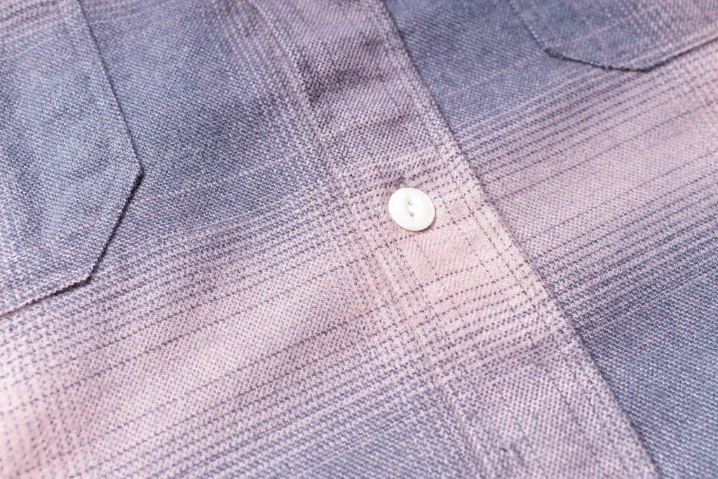 Close-up of a textured fabric with a button on a checkered shirt.