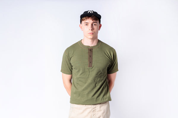 Man wearing a green shirt and beige pants against a white background