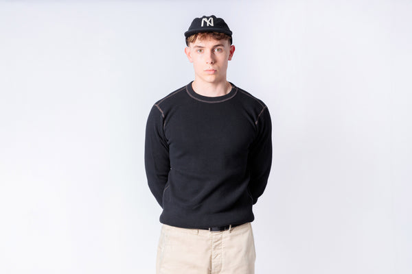 Person wearing a black sweater and beige pants against a white background