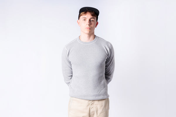 Person wearing a gray sweater and beige pants against a white background