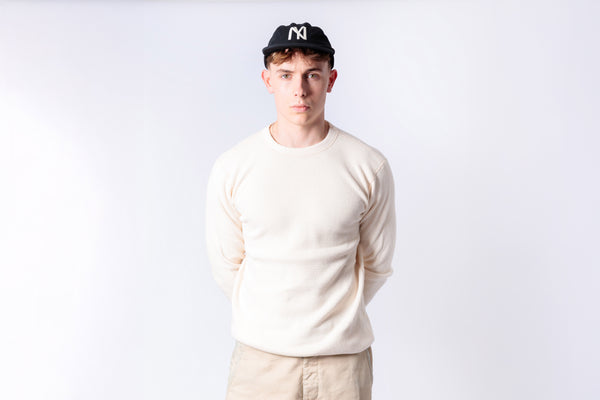 Person wearing a white sweater and beige pants with a black cap on a white background