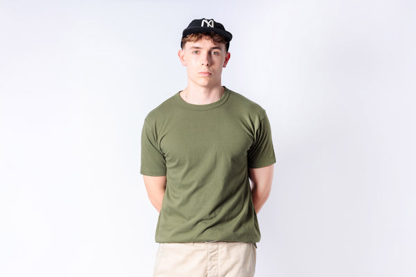 Person wearing an olive green t-shirt and beige pants against a white background