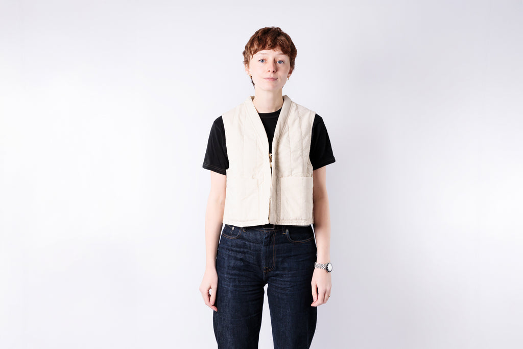 Person wearing a beige vest over a black shirt on a white background