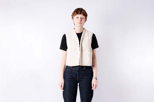 Person wearing a beige vest over a black shirt on a white background