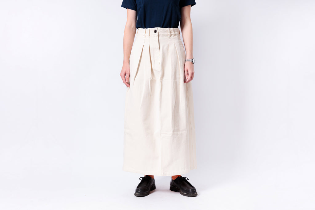 Person wearing a long beige skirt with a plain background