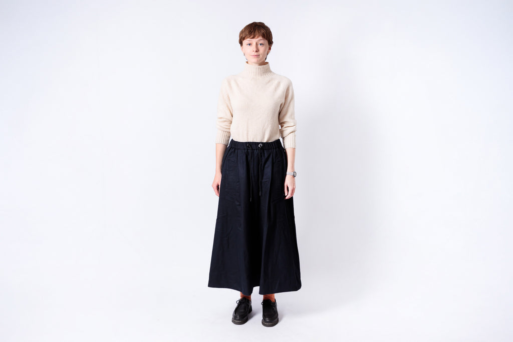 Person wearing a beige turtleneck and black skirt on a white background