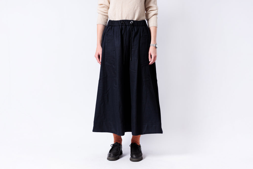 Person wearing a black skirt and beige sweater on a white background