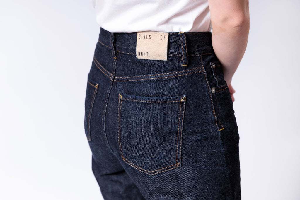 Person wearing dark blue jeans with a visible brand label on a white background