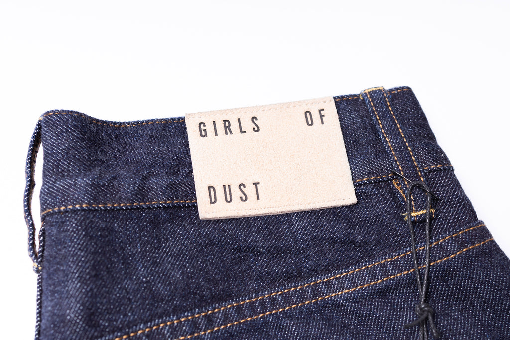 Close-up of blue denim jeans with a 'Girls of Dust' label on a white background