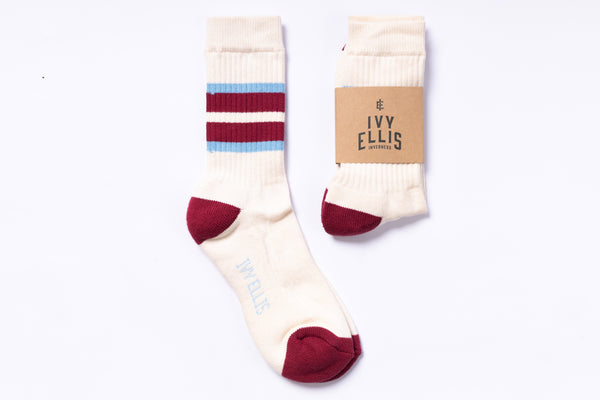 Pair of cream socks with red toes and heels, striped blue and red on leg, next to a brown cardboard sleeve with 'Ivy Ellis' branding on a white background.