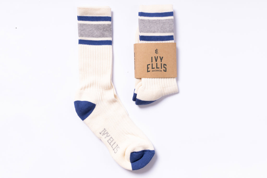 Pair of cream socks with blue accents and a cardboard packaging label on a white background