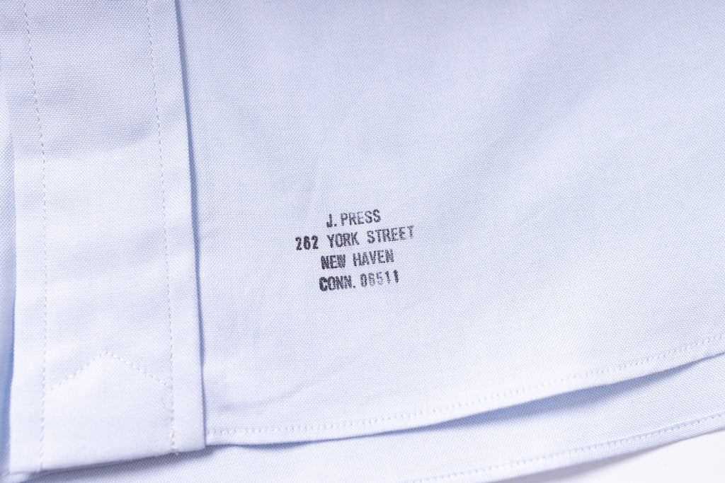 Close-up of a white shirt with black text on the collar, showing 'J. Press' and address details.