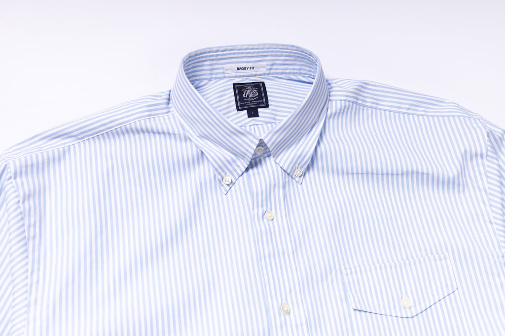 Folded blue and white striped dress shirt with a brand label on a light gray background
