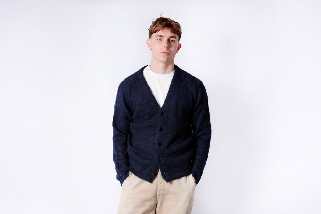 Man wearing a navy cardigan over a white shirt with beige pants on a white background