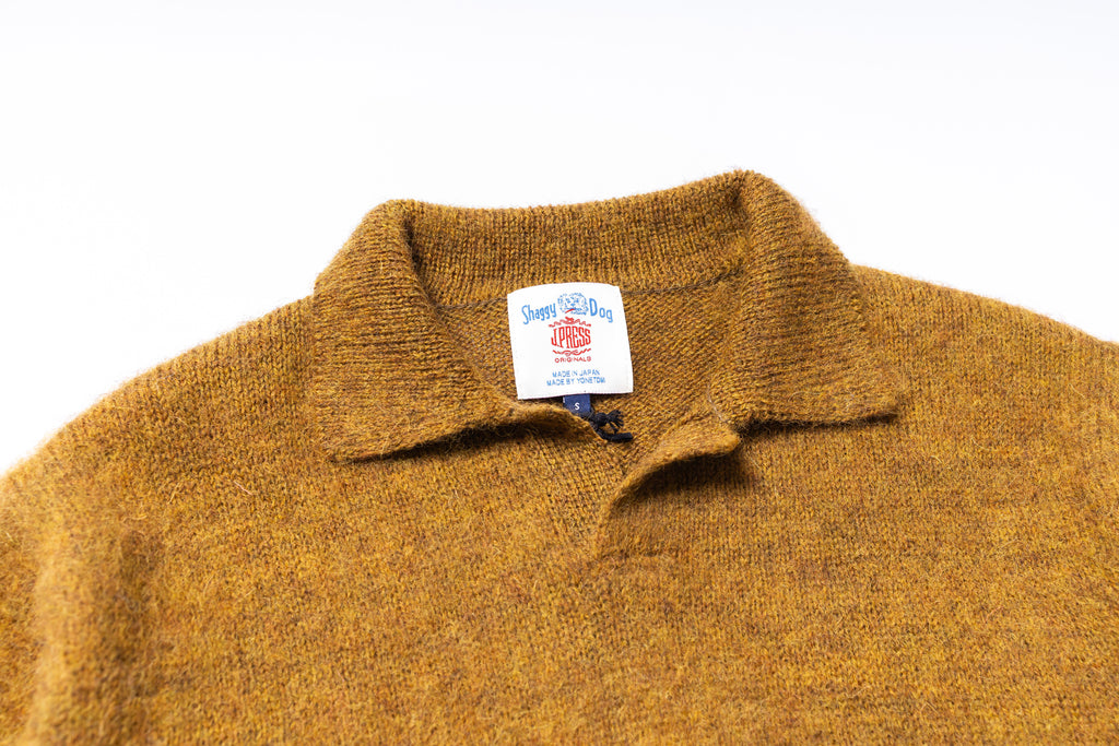 Close-up of a mustard yellow sweater with a brand label on a white background