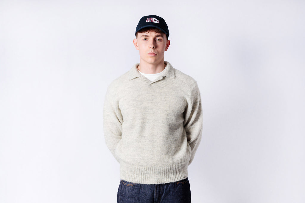 Person wearing a light gray sweater and dark cap on a white background