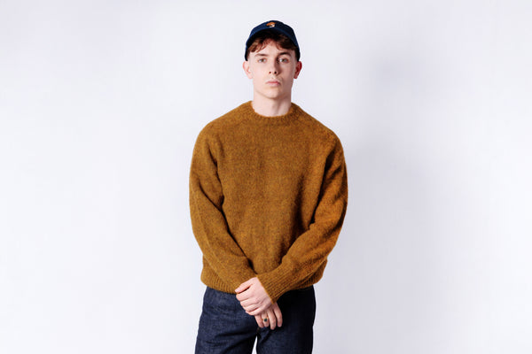 Person wearing a mustard yellow sweater and dark cap on a white background