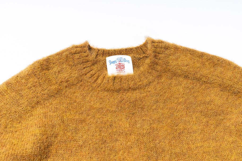 Close-up of a mustard yellow sweater with a brand label on a white background