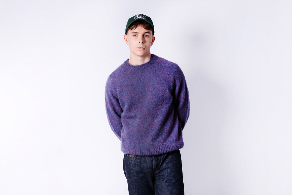 Person wearing a purple sweater and dark pants against a white background