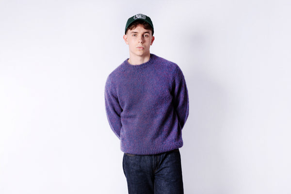 Person wearing a purple sweater and dark pants against a white background