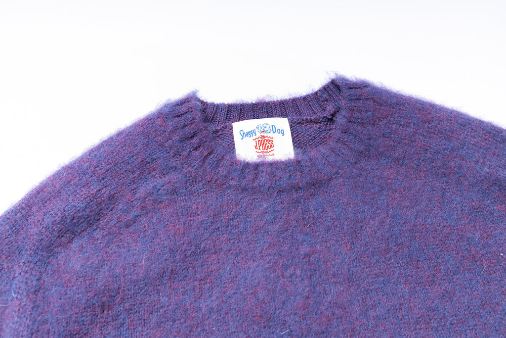 Close-up of a purple sweater with a brand label on a white background