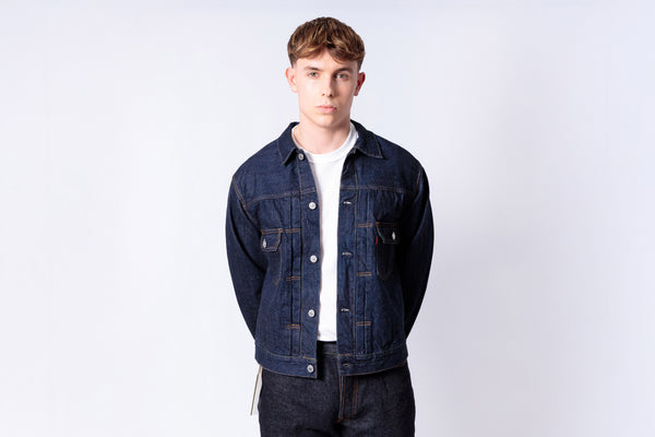 Man wearing a denim jacket over a white shirt on a light gray background