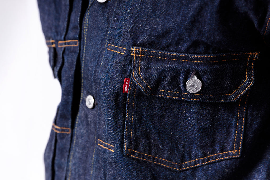 Close-up of a blue denim jacket with a brand logo on the chest pocket.