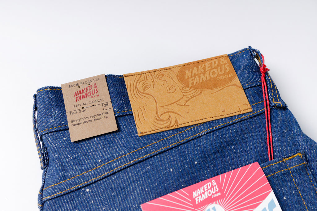 Close-up of blue jeans with 'Naked & Famous' label on a white background