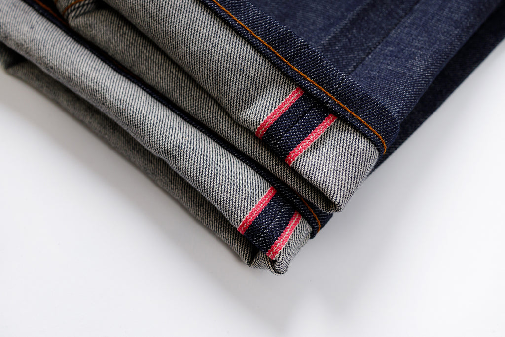 Stack of folded jeans with visible stitching details on a white background