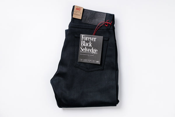 Folded black selvage denim jeans with a tag on a white background