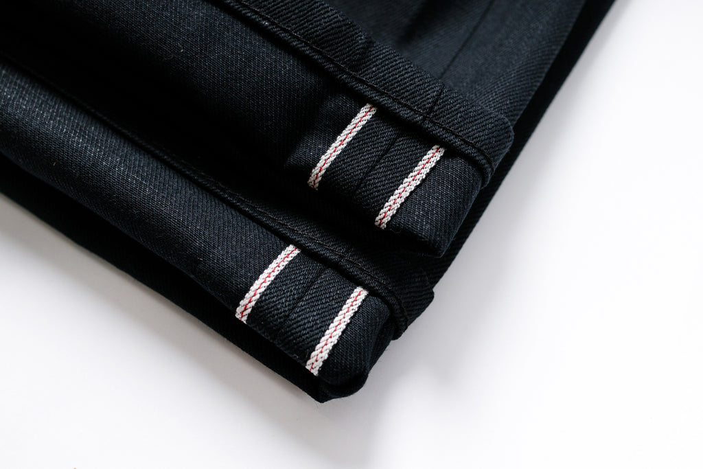 Folded black fabric with pink stitching on a white background