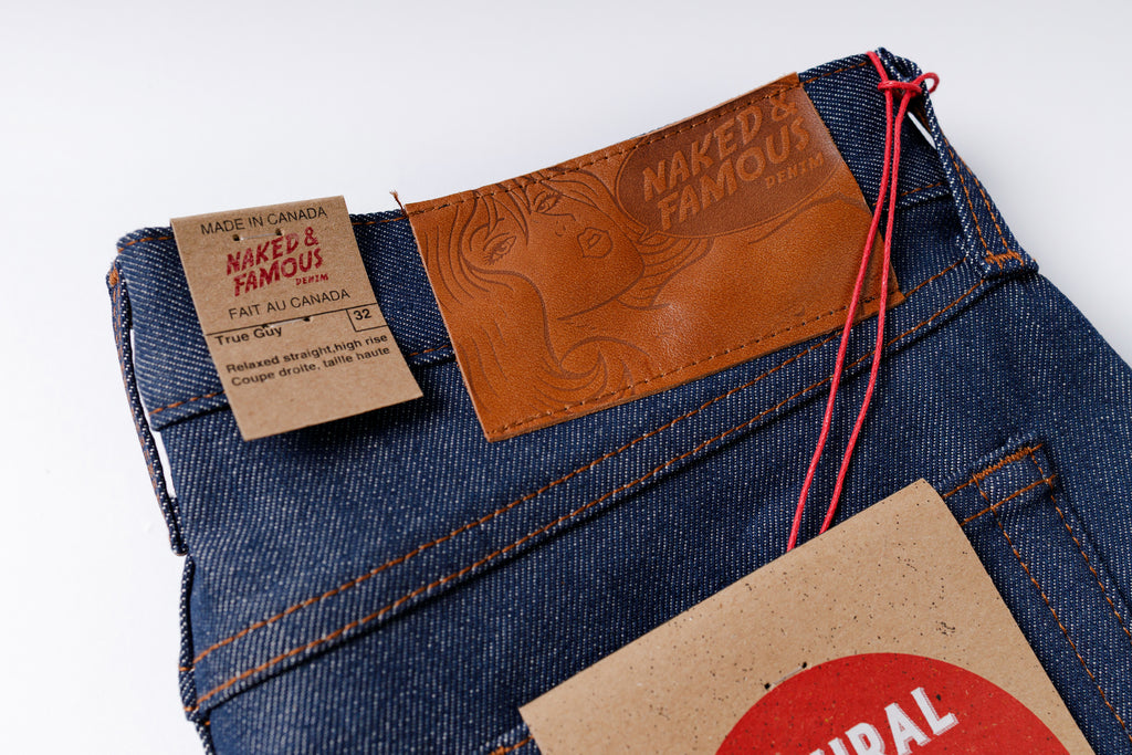 Close-up of blue jeans with 'Naked & Famous' branding on a white background