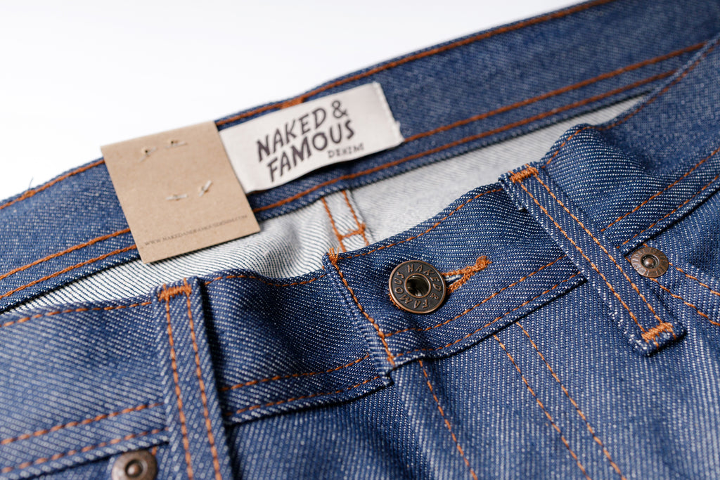 Close-up of blue jeans with a 'Naked & Famous' label on a white background