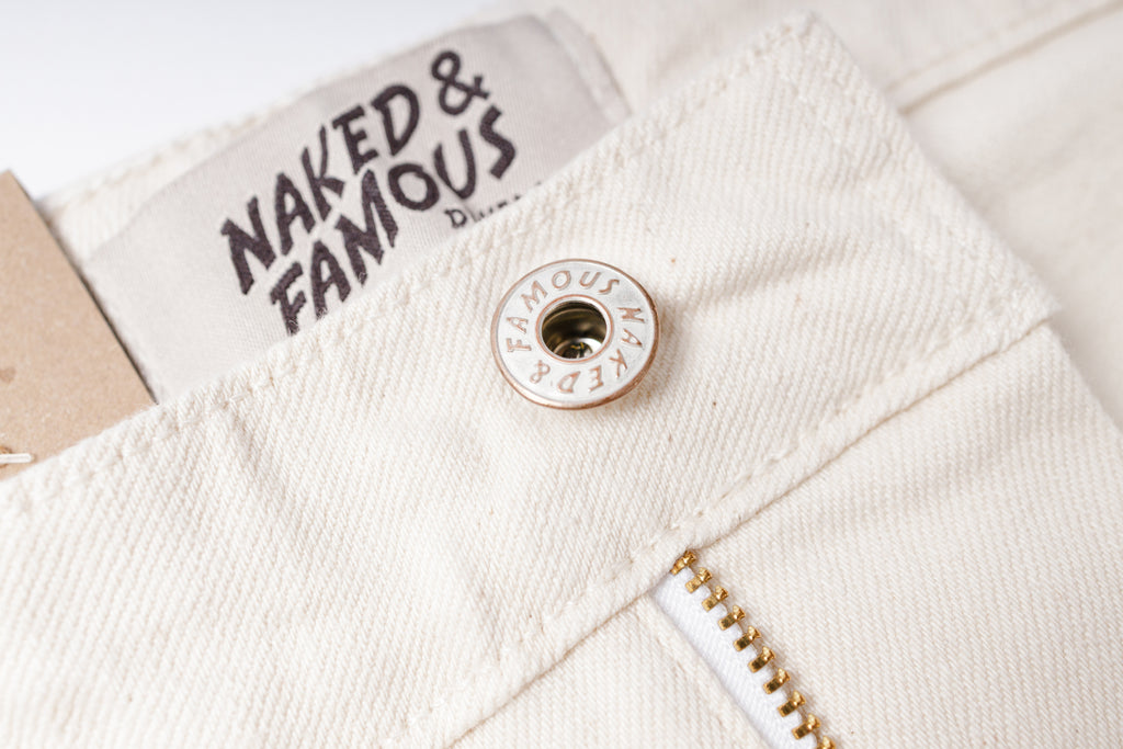 Close-up of a button on a white denim jacket with 'Naked & Famous' branding.