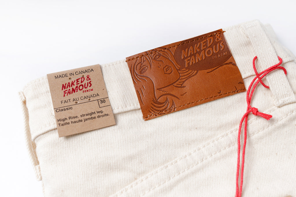 Close-up of white jeans with 'Naked & Famous' label on a white background