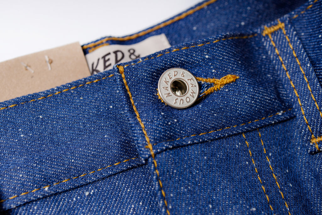 Close-up of a button on blue denim fabric with branding.