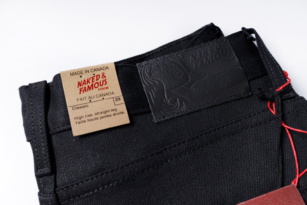 Black jeans with 'Naked & Famous' label and branding details on a white background