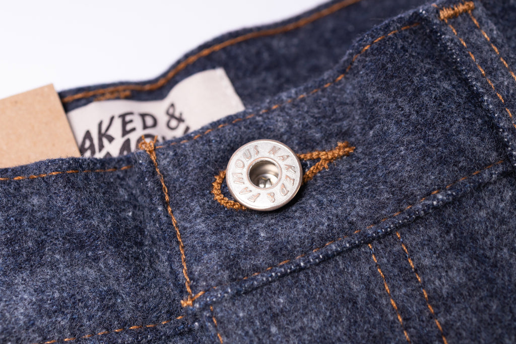 Close-up of a button on blue denim fabric with a brand label in the background.