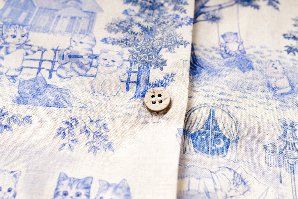 Close-up of fabric with blue and white pattern featuring houses and bears, with a button in the center.