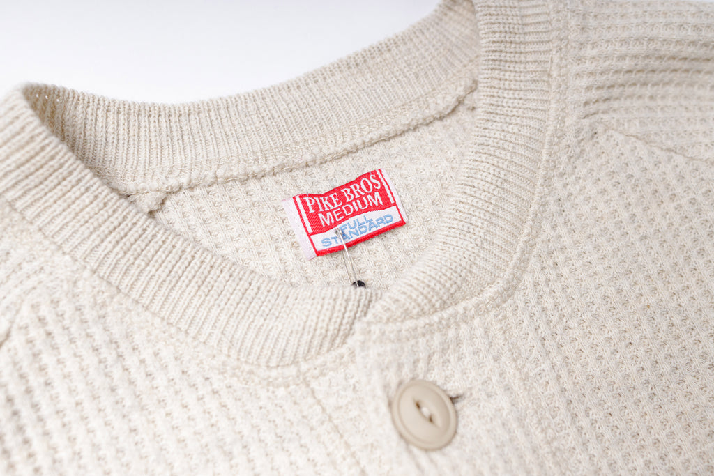 Close-up of a beige sweater with a red label on a white background